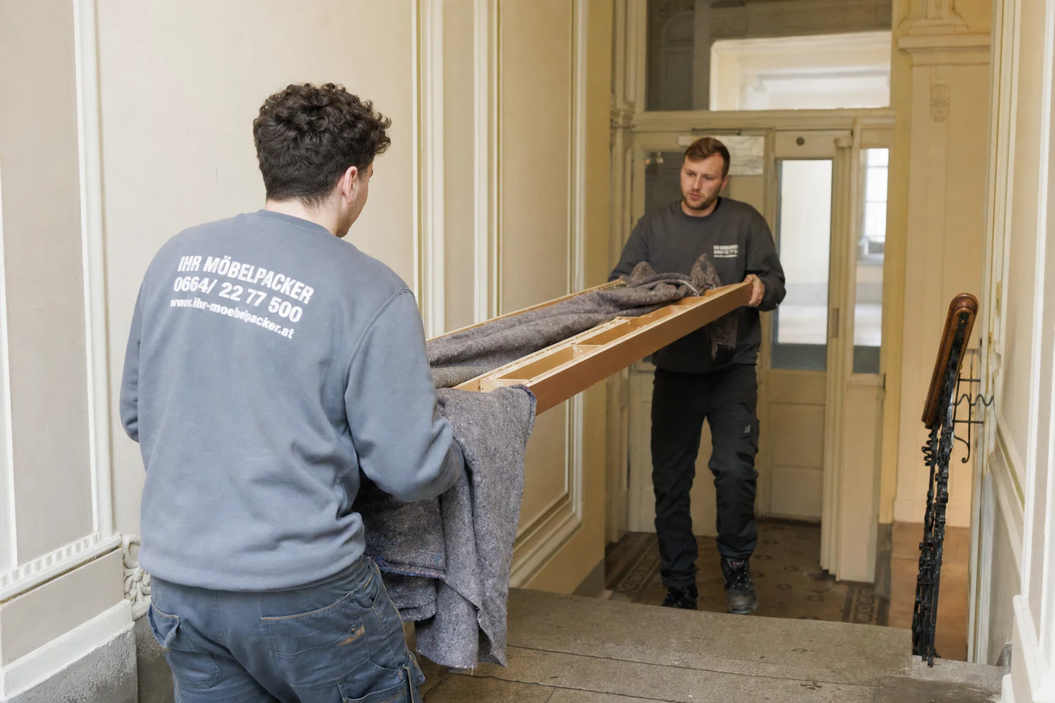 Demontage Wien – zwei Mitarbeiter tragen zerlegtes Möbelteil durch Wiener Altbau-Stiegenhaus